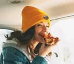 woman wearing a yellow beanie eating pizza