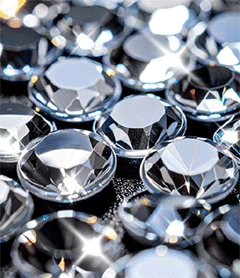 High-resolution macro shot of individual clear faceted crystal rhinestones used for heat transfer apparel decoration and sparkling garment embellishments.